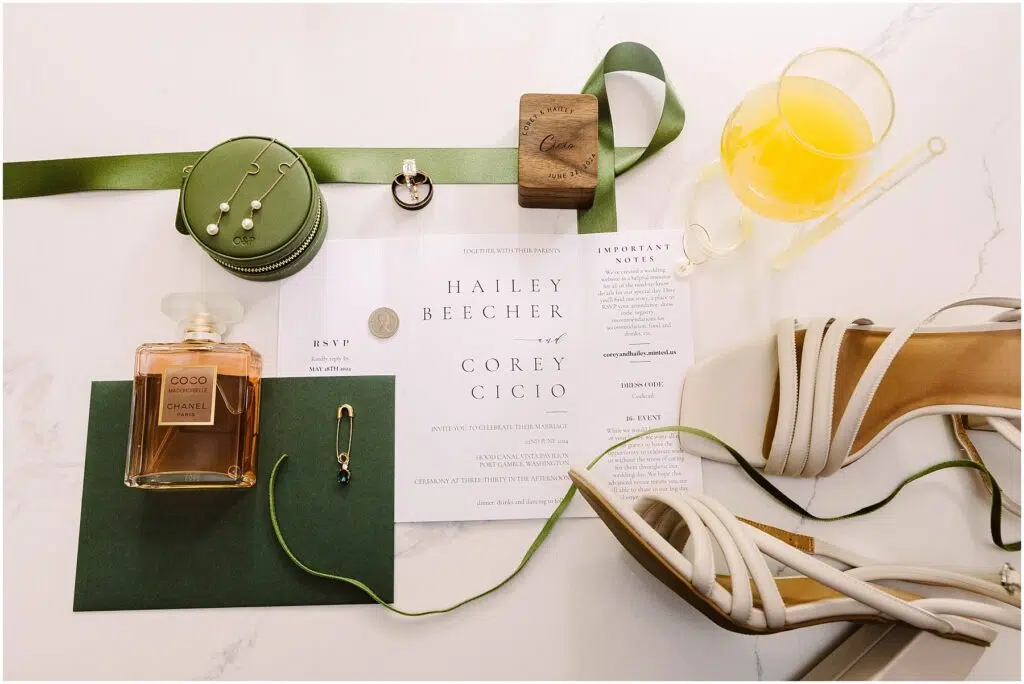 Snohomish Wedding Photographer GSquared Weddings Invitation set for Hailey Beecher and Corey Cicio features delicate perfume, green ribbon, pearl earrings, and a wooden item. An orange drink with a stirring stick complements this Port Gamble affair. Perfect touches for a Summer Wedding; RSVP and important notes included. Serving Seattle, Snohomish and Orlando