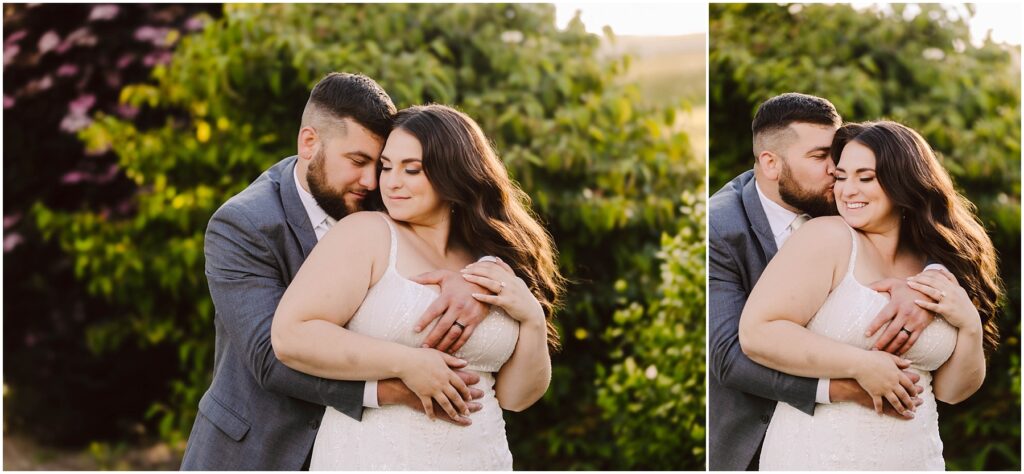 Snohomish Wedding Photographer GSquared Weddings In the heart of Port Gamble, amidst lush greenery, a couple embraces warmly. The man, in a gray suit, hugs the woman in her white dress from behind. Their content expressions and the soft summer wedding sunlight illuminate the serene scene. Serving Seattle, Snohomish and Orlando