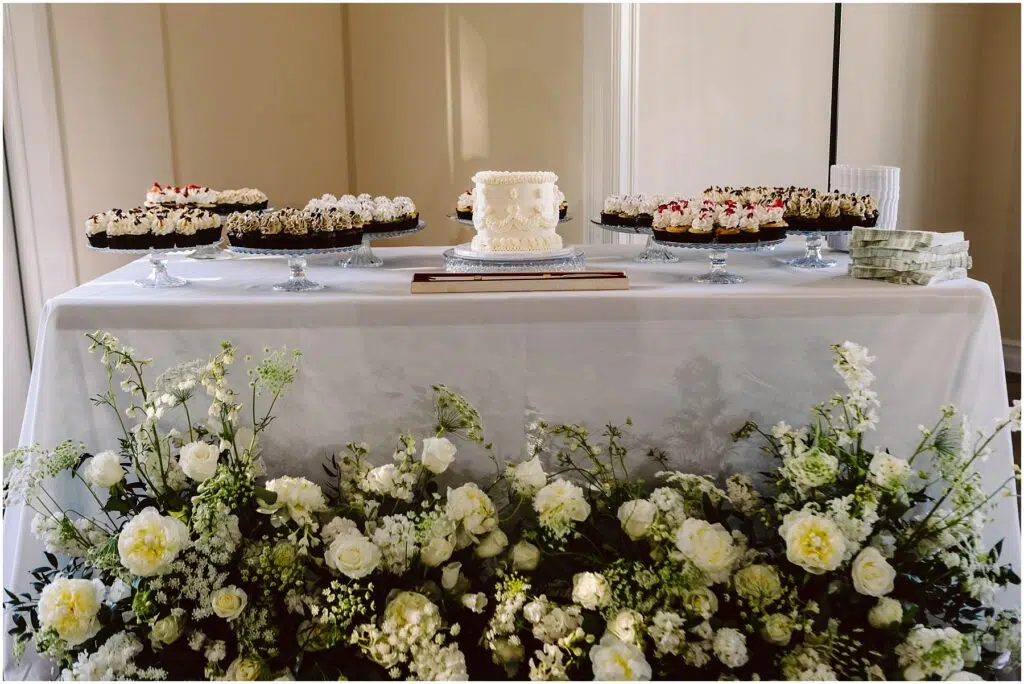 Snohomish Wedding Photographer GSquared Weddings At a charming Port Gamble summer wedding, a dessert table features a small white cake at its center, surrounded by an array of cupcakes displayed on glass stands. The setup is enhanced with a pristine white cloth and an elegant arrangement of white flowers gracing the front. Serving Seattle, Snohomish and Orlando