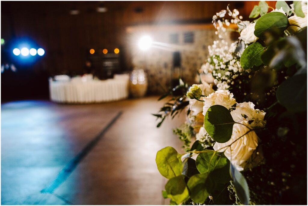 Snohomish Wedding Photographer GSquared Weddings A warmly lit event space with blurred ambient lights in the background. A bouquet of white and cream roses with greenery is prominently displayed in the foreground, evoking the charm of a winery setting. The atmosphere suggests a celebratory occasion. Serving Seattle, Snohomish and Orlando