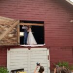 Snohomish Wedding Photographer GSquared Weddings A bride and groom share a kiss in the loft of a red barn as a photographer and guests capture the moment from below. The scene is festive with rustic décor and greenery nearby. Serving Seattle, Snohomish and Orlando