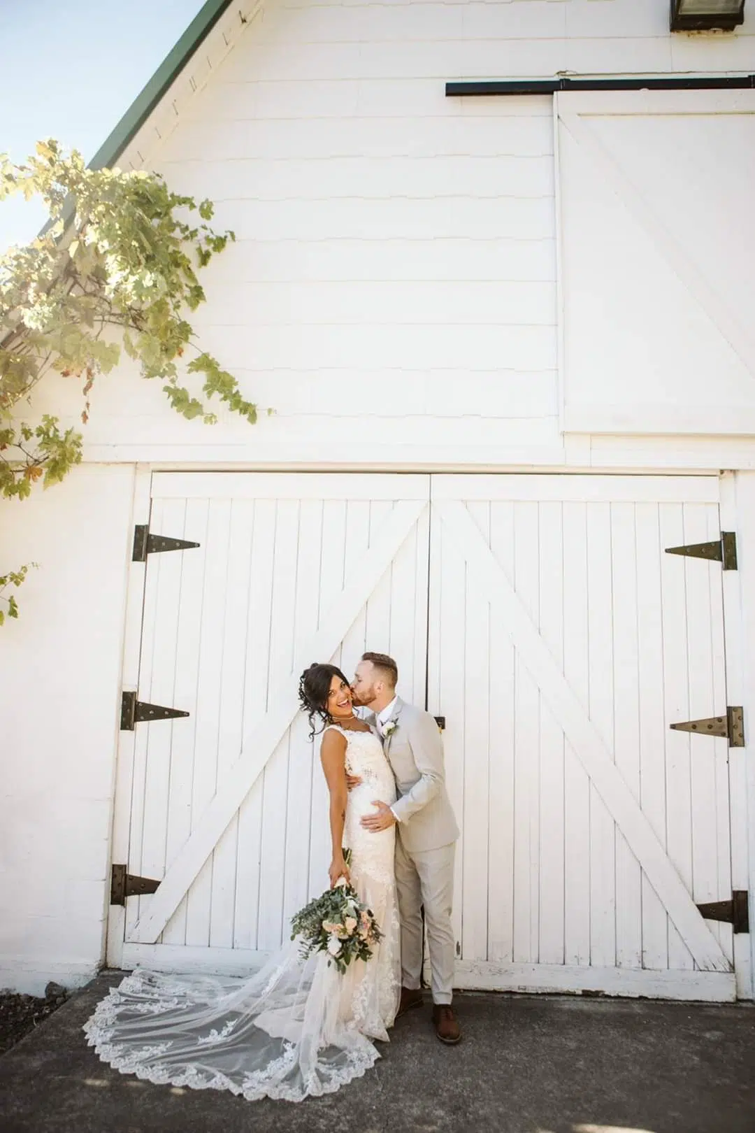 Snohomish Wedding Photographer GSquared Weddings A bride and groom share a kiss in front of large white barn doors The bride holds a bouquet and wears a lace dress with a long train while the groom is dressed in a lightcolored suit Sunlight casts a soft glow Serving Seattle Snohomish and Orlando Snohomish Wedding Photographer GSquared Weddings A bride and groom share a kiss in front of large white barn doors The bride holds a bouquet and wears a lace dress with a long train while the groom is dressed in a light colored suit Sunlight casts a soft glow Serving Seattle Snohomish and Orlando
