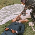 Snohomish Wedding Photographer GSquared Weddings A bride and groom lie on the grass with eyes closed, her veil spread out behind them. A woman with purple hair adjusts the bride’s position. A bouquet lies nearby on the grass. Serving Seattle, Snohomish and Orlando