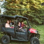 Snohomish Wedding Photographer GSquared Weddings Four people sit and smile in a black and red off-road ATV parked on grass, with tall green pine trees in the background. Sunlight filters through the trees, creating a warm, cheerful atmosphere. Serving Seattle, Snohomish and Orlando