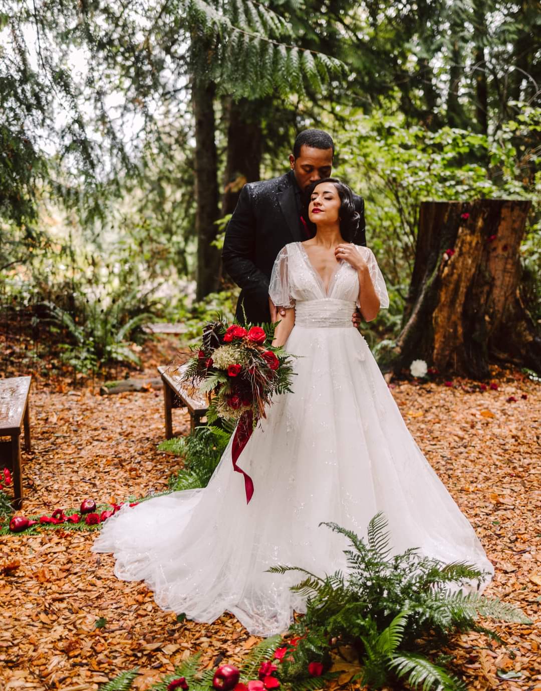 Snohomish Wedding Photographer GSquared Weddings A bride in a white gown holds a bouquet of red flowers while standing in a forest with the groom standing behind her gently embracing her Leaves ferns and red flowers decorate the natural setting Serving Seattle Snohomish and Orlando Snohomish Wedding Photographer GSquared Weddings A bride in a white gown holds a bouquet of red flowers while standing in a forest with the groom standing behind her gently embracing her Leaves ferns and red flowers decorate the natural setting Serving Seattle Snohomish and Orlando