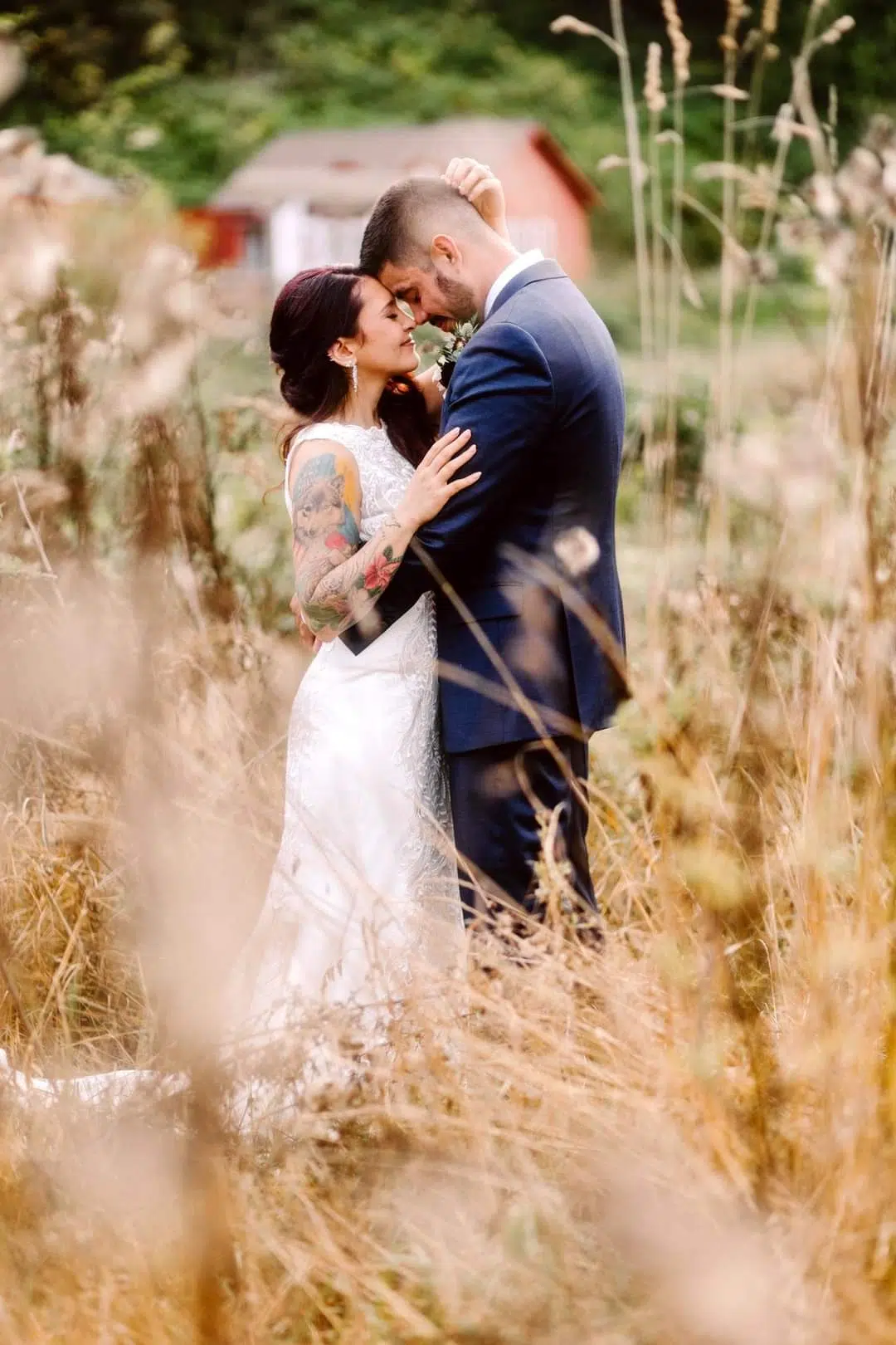 Snohomish Wedding Photographer GSquared Weddings A bride and groom embrace lovingly in a field of tall grass surrounded by dried wildflowers The bride has visible tattoos and wears a lace dress while the groom is in a navy suit A red building is blurred in the background Serving Seattle Snohomish and Orlando Snohomish Wedding Photographer GSquared Weddings A bride and groom embrace lovingly in a field of tall grass surrounded by dried wildflowers The bride has visible tattoos and wears a lace dress while the groom is in a navy suit A red building is blurred in the background Serving Seattle Snohomish and Orlando