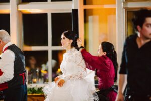 Snohomish Wedding Photographer GSquared Weddings A woman in a white lace wedding dress is being assisted by another woman in a red dress, adjusting her hair. They are indoors, with warm lighting and large windows in the background. Serving Seattle, Snohomish and Orlando