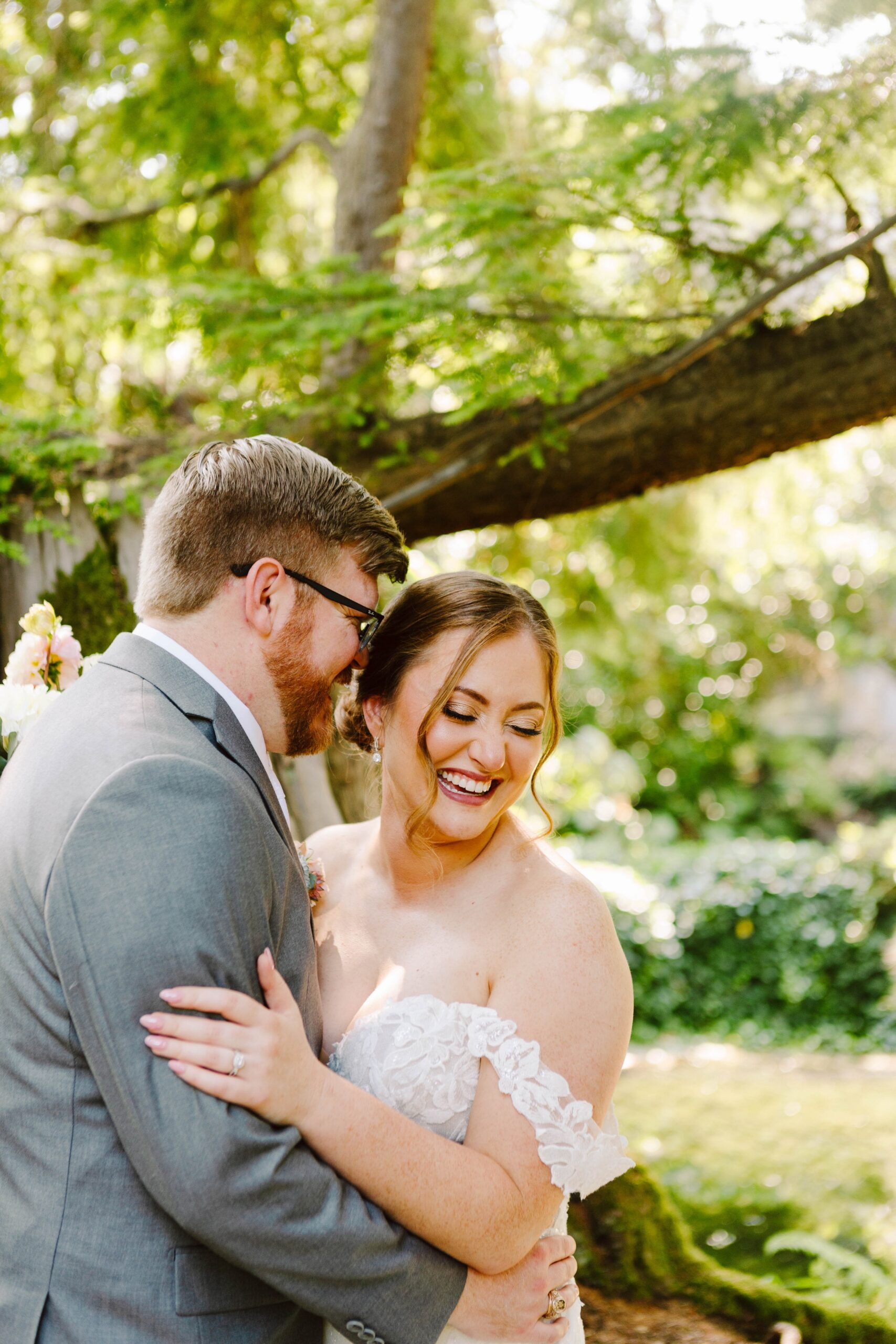 Snohomish Wedding Photographer GSquared Weddings A bride and groom embrace and smile joyfully outdoors under a tree, surrounded by greenery and dappled sunlight. Captured by GSquared Weddings, this Snohomish wedding photography moment radiates romance and natural charm. Serving Seattle, Snohomish and Orlando