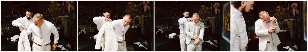 Snohomish Wedding Photographer GSquared Weddings In a dimly lit room adorned with colorful wall art, two men stand together. One, wearing a suit, assists the other in donning a white jacket. As they adjust it and inspect the sleeve, the air carries an aura reminiscent of Snohomish’s quiet charm. Serving Seattle, Snohomish and Orlando