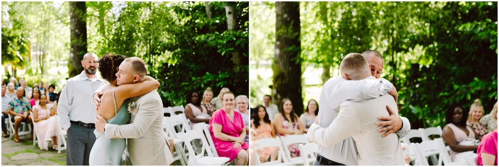 Snohomish Wedding Photographer GSquared Weddings Two people embrace in a heartfelt hug amidst the lush, green landscapes of Snohomish, surrounded by wedding guests seated outdoors. Another person looks on with a gentle smile. Serving Seattle, Snohomish and Orlando