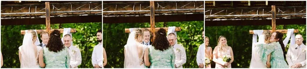 Snohomish Wedding Photographer GSquared Weddings In the serene setting of Snohomish, a bride and groom stand before a wooden cross, joined by two companions. One, in a light green dress, offers an embrace. Towering trees and a rustic wooden structure frame this picturesque moment. Serving Seattle, Snohomish and Orlando