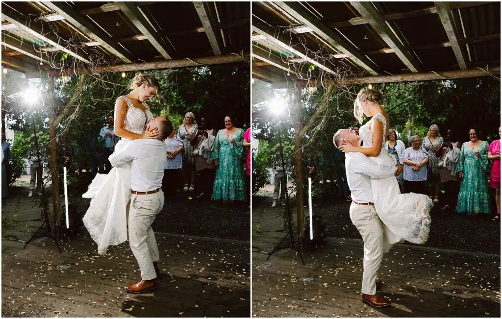 Snohomish Wedding Photographer GSquared Weddings A groom lifts the bride joyfully under a wooden pergola in Snohomish. Guests stand in the background, smiling. The bride wears a white gown, and the groom is in light-colored attire. The scene is festive with string lights and scattered petals. Serving Seattle, Snohomish and Orlando