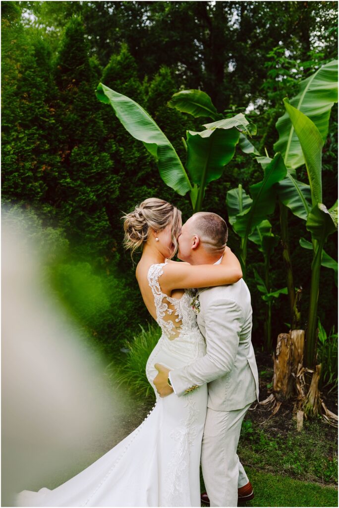 Snohomish Wedding Photographer GSquared Weddings A groom in a light suit joyfully lifts and kisses the bride, adorned in a lace wedding dress. They stand amidst lush greenery and large tropical leaves, crafting a romantic atmosphere that feels straight out of Snohomishs enchanting landscapes. Serving Seattle, Snohomish and Orlando