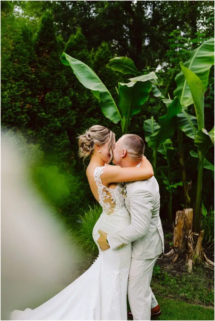 Snohomish Wedding Photographer GSquared Weddings A groom in a light suit joyfully lifts and kisses the bride, adorned in a lace wedding dress. They stand amidst lush greenery and large tropical leaves, crafting a romantic atmosphere that feels straight out of Snohomishs enchanting landscapes. Serving Seattle, Snohomish and Orlando