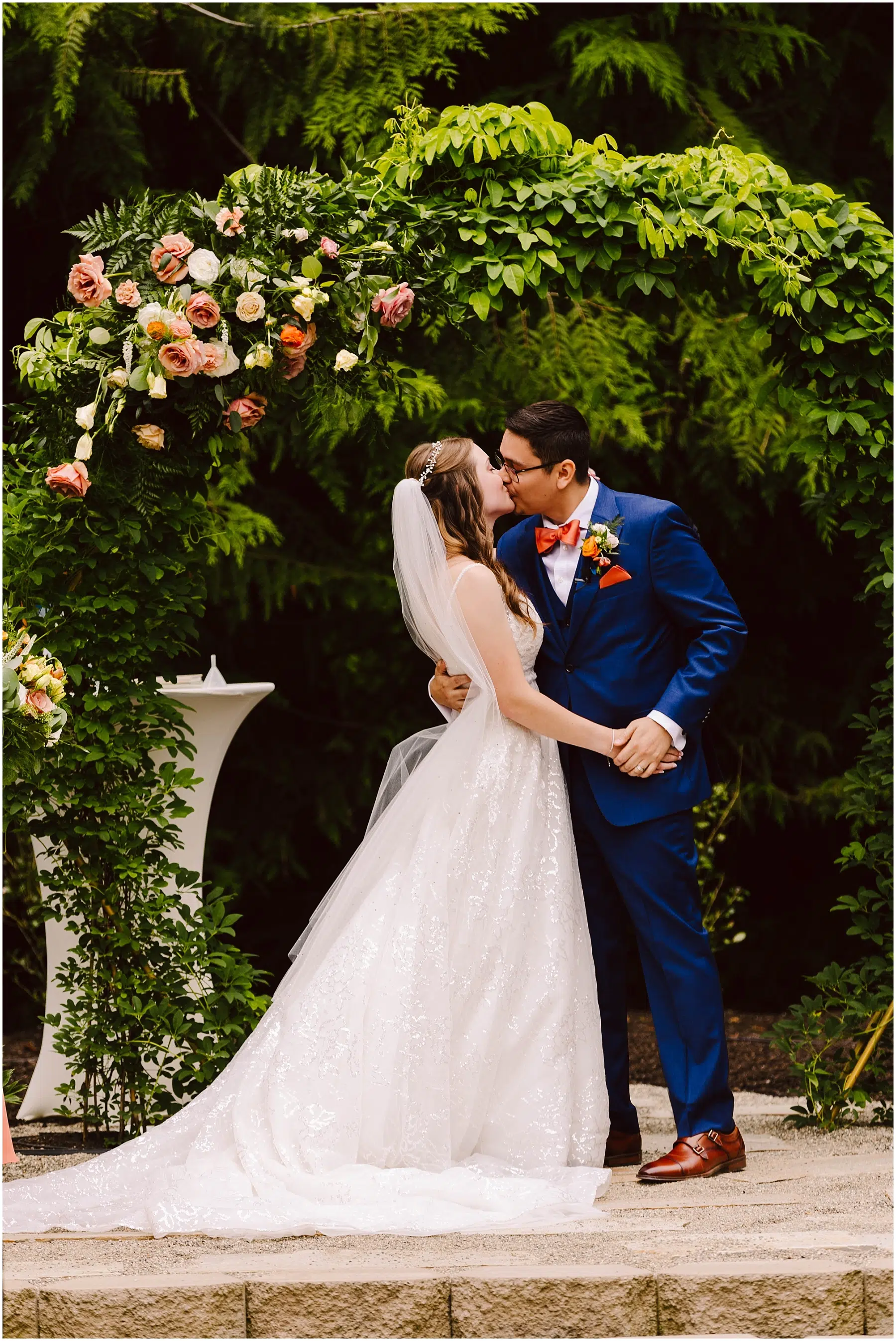 Snohomish Wedding Photographer GSquared Weddings In a charming backyard wedding in Stanwood a bride in a white gown and veil kisses her groom who dons a blue suit and red bow tie They stand under a floral arch adorned with pink and white blossoms embraced by lush greenery Serving Seattle Snohomish and Orlando Snohomish Wedding Photographer GSquared Weddings In a charming backyard wedding in Stanwood a bride in a white gown and veil kisses her groom who dons a blue suit and red bow tie They stand under a floral arch adorned with pink and white blossoms embraced by lush greenery Serving Seattle Snohomish and Orlando