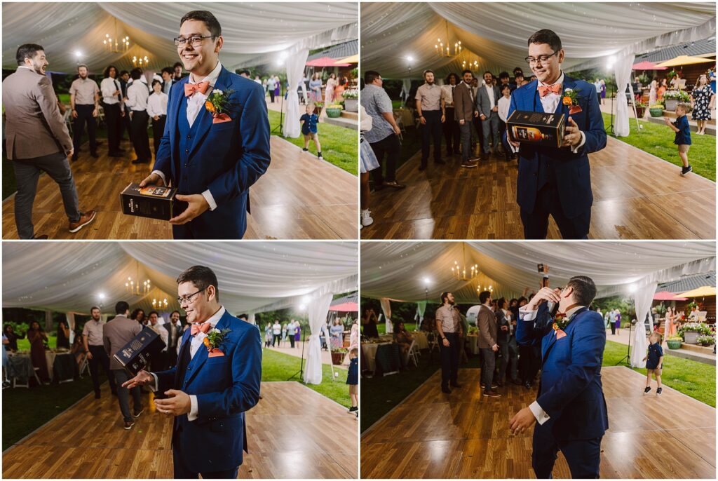 Snohomish Wedding Photographer GSquared Weddings A man in a blue suit with a boutonniere stands in a tented outdoor area, likely at a backyard wedding, holding a black box. He gestures animatedly to an attentive group. The wooden ground hints at the festive mood, as attendees enjoy the celebration dressed in formal attire. Serving Seattle, Snohomish and Orlando