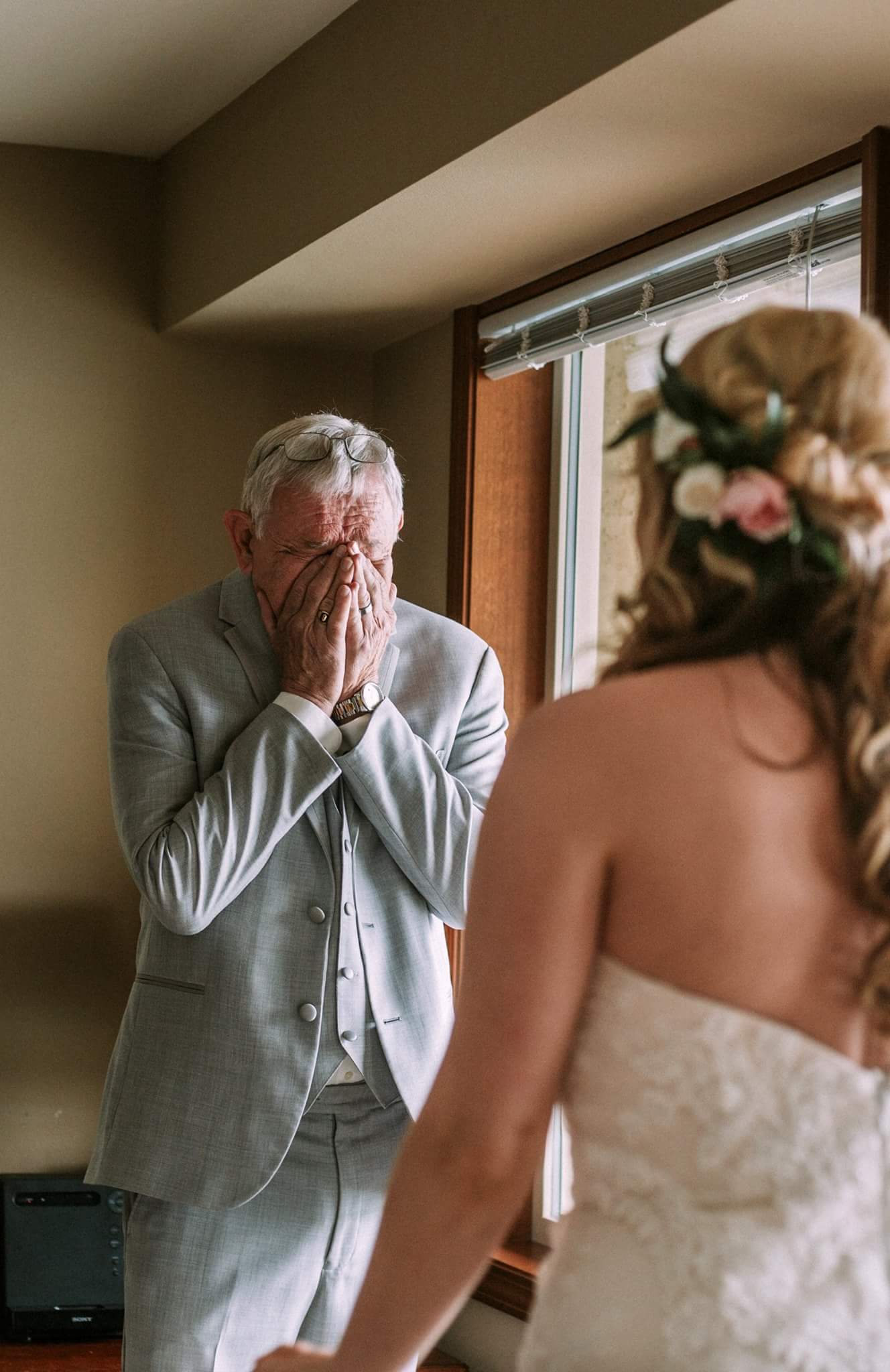 GSquared Weddings Photography A man in a light gray suit covers his face with emotion as he witnesses a woman in a strapless wedding dress, flowers in her hair, standing by a window in the softly lit room. 47.9129° N, 122.0982° W | Serving Snohomish, Seattle , Orlando & Beyond