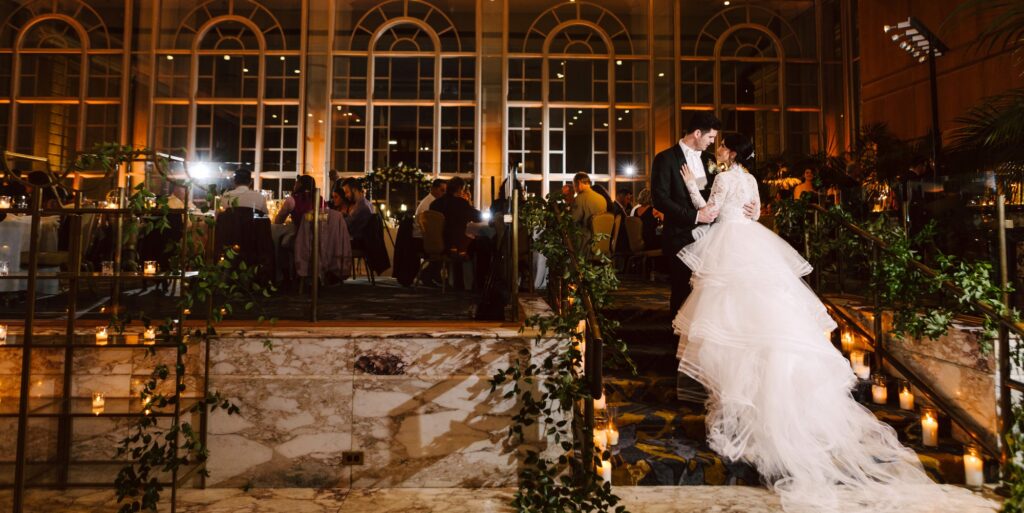 GSquared Weddings Photography A bride in a flowing white gown and a groom in a suit share a romantic moment at the base of candlelit marble stairs during an elegant evening wedding reception in a grand hall, perfect for featuring on an Elementor Thank You page. GSquared Weddings | 47.9129° N, 122.0982° W | Serving Snohomish, Seattle , Orlando & Beyond