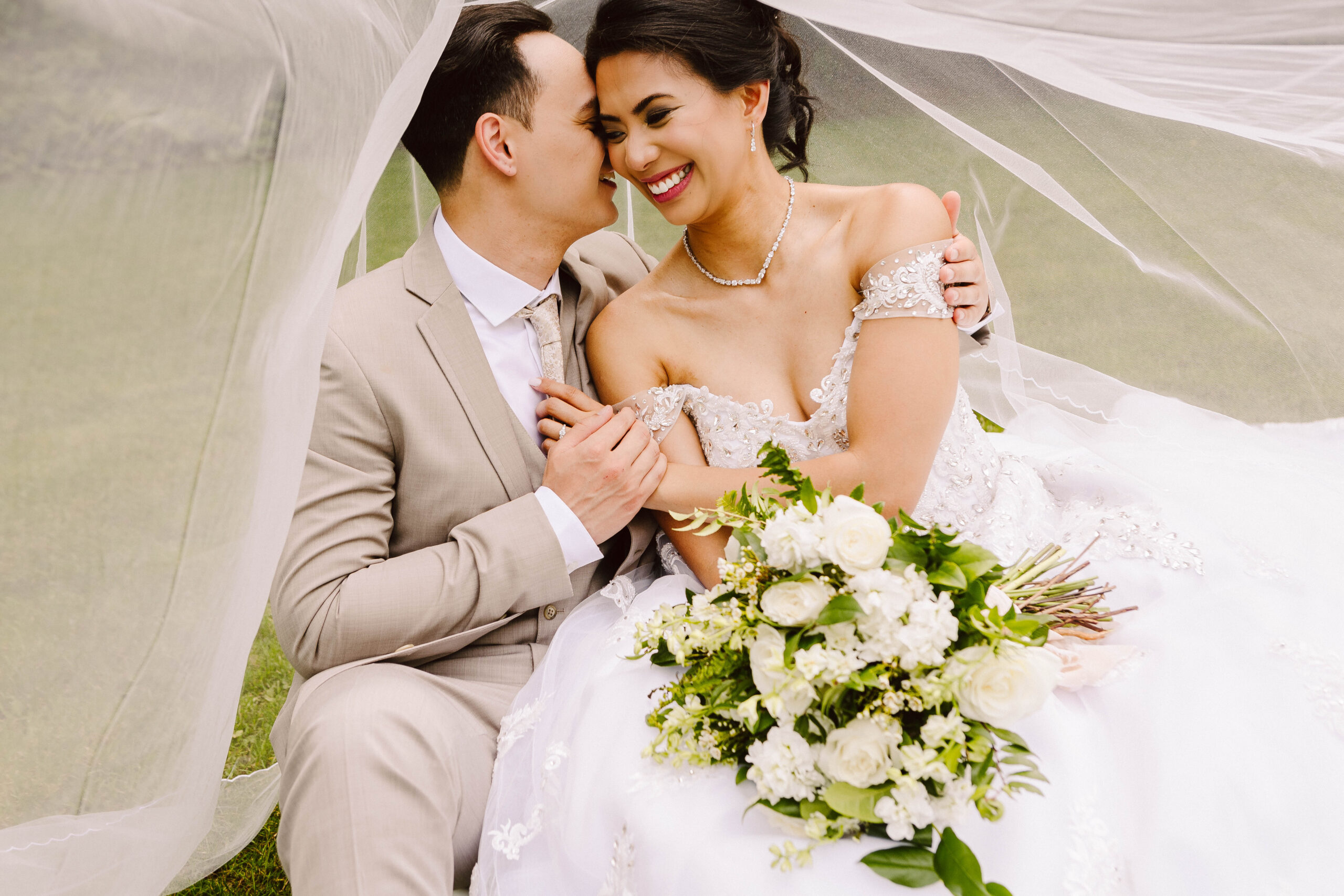 GSquared Weddings Photography A bride and groom sit closely under a veil, smiling and holding hands. Perfect for an Elementor home page, this joyful couple—she in white with a bouquet, he in a light suit—radiate love and happiness, ready to inspire your website builder project. GSquared Weddings | 47.9129° N, 122.0982° W | Serving Snohomish, Seattle , Orlando & Beyond