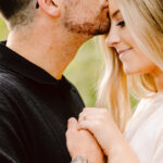 GSquared Weddings Photography A man kisses a womans forehead as she smiles with her eyes closed, holding his hand and showing an engagement ring. The man has short hair, glasses, and a tattoo on his arm. 47.9129° N, 122.0982° W | Serving Snohomish, Seattle , Orlando & Beyond