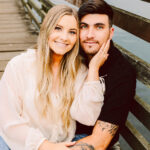 GSquared Weddings Photography A smiling couple sits closely together on a wooden boardwalk by the water. The woman has long blonde hair and lightly touches the mans cheek, while he has dark hair and an arm with tattoos resting on her knee. 47.9129° N, 122.0982° W | Serving Snohomish, Seattle , Orlando & Beyond
