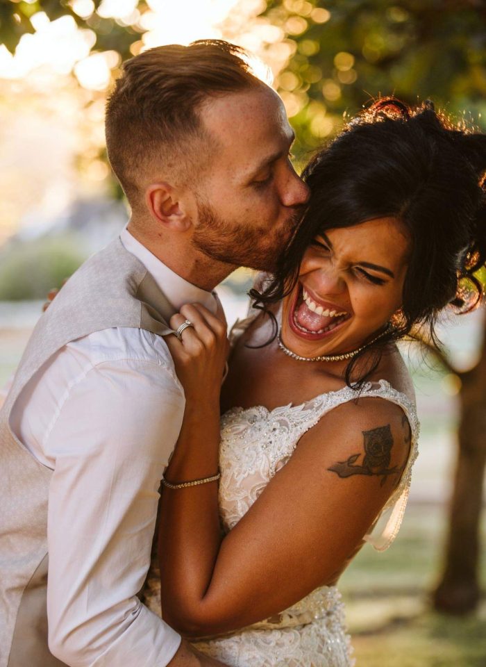 GSquared Weddings Photography A groom kisses his smiling bride on the forehead during an outdoor wedding, both dressed in formal attire and illuminated by warm sunlight—a moment as beautifully crafted as a WordPress site with expert Elementor services. GSquared Weddings | 47.9129° N, 122.0982° W | Serving Snohomish, Seattle , Orlando & Beyond