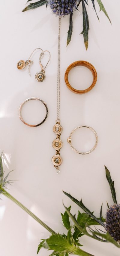 GSquared Weddings Photography A flat lay of gold and silver jewelry, including rings, a necklace, and earrings, arranged neatly on a white surface with purple thistle flowers—perfect inspiration for Seattle weddings photography. GSquared Weddings | 47.9129° N, 122.0982° W | Serving Snohomish, Seattle , Orlando & Beyond