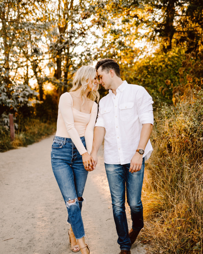 GSquared Weddings Photography A couple walks hand in hand on a dirt path surrounded by trees at sunset, smiling and leaning their heads together, dressed in casual jeans and light-colored tops—perfect inspiration for authentic Elementor Design. GSquared Weddings | 47.9129° N, 122.0982° W | Serving Snohomish, Seattle , Orlando & Beyond