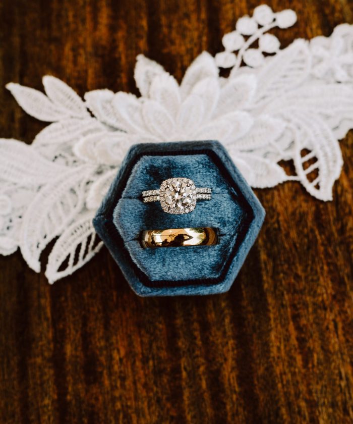 GSquared Weddings Photography A hexagonal blue ring box holds a diamond engagement ring and a gold wedding band, placed on a wooden surface with a piece of white lace in the background—perfect for showcasing on your WordPress site with Elementor services. GSquared Weddings | 47.9129° N, 122.0982° W | Serving Snohomish, Seattle , Orlando & Beyond