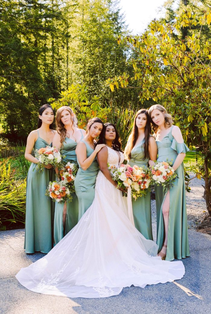 Snohomish Wedding Photographer GSquared Weddings A bride in a white gown stands outdoors with five bridesmaids in sage green dresses, all holding colorful bouquets, posing together in natural sunlight surrounded by greenery. Serving Seattle, Snohomish and Orlando