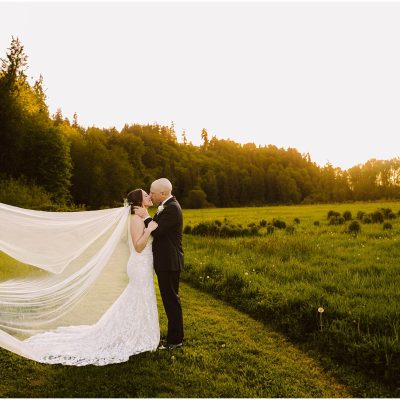 Snohomish Wedding Photographer GSquared Weddings A bride and groom stand in a grassy field at sunset, surrounded by trees. The bride wears a long, flowing veil, and the couple embraces, facing each other, with golden sunlight illuminating the scene. Serving Seattle, Snohomish and Orlando