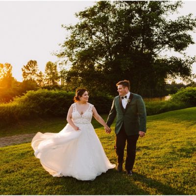 Glam Wedding at Pemberton Farm bride and groom walking in the sunset on the grass with a tree and river behind them illuminated by warm glowing evening light